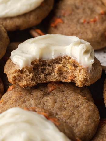 Several carrot cake cookies laying around each other. The top cookie has a bite missing.