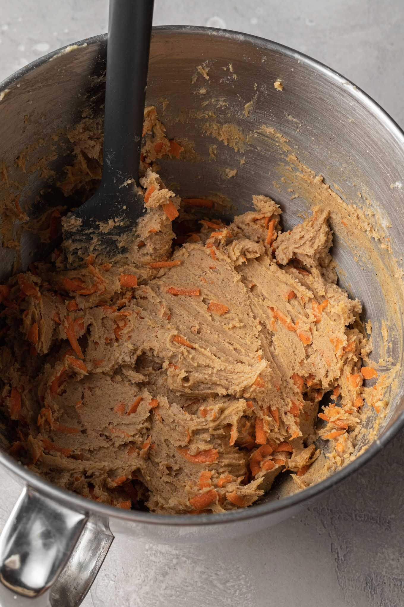 Raw carrot cake cookie dough in a metal mixing bowl with a rubber spatula. 