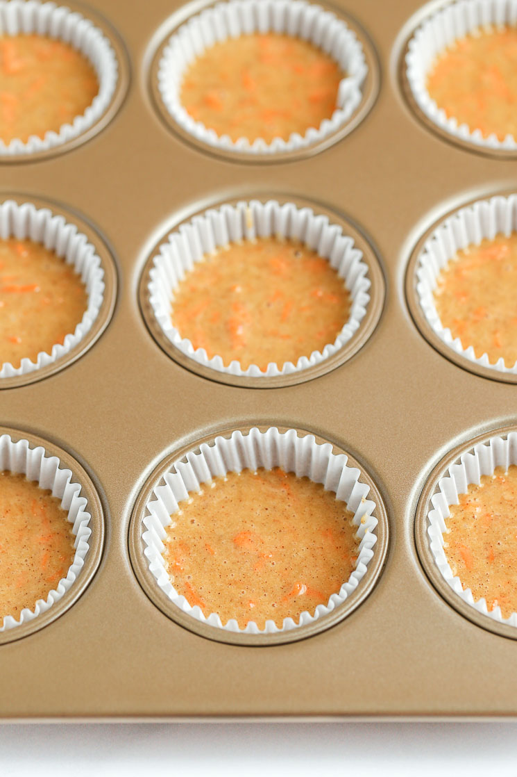 A muffin pan filled with cupcake liners and carrot cake cupcake batter.