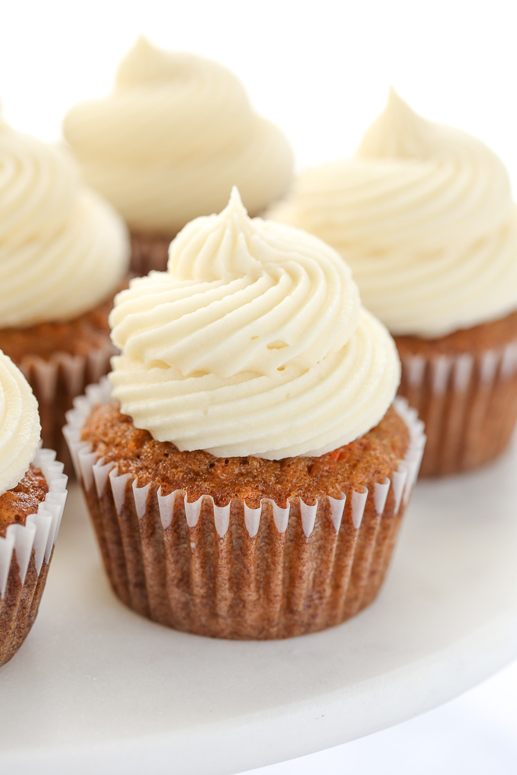 A close up picture of carrot cake cupcakes topped with cream cheese frosting sitting on top of a marble cake stand. 