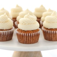 A group of carrot cake cupcakes topped with cream cheese frosting setting on top of a marble cake stand.