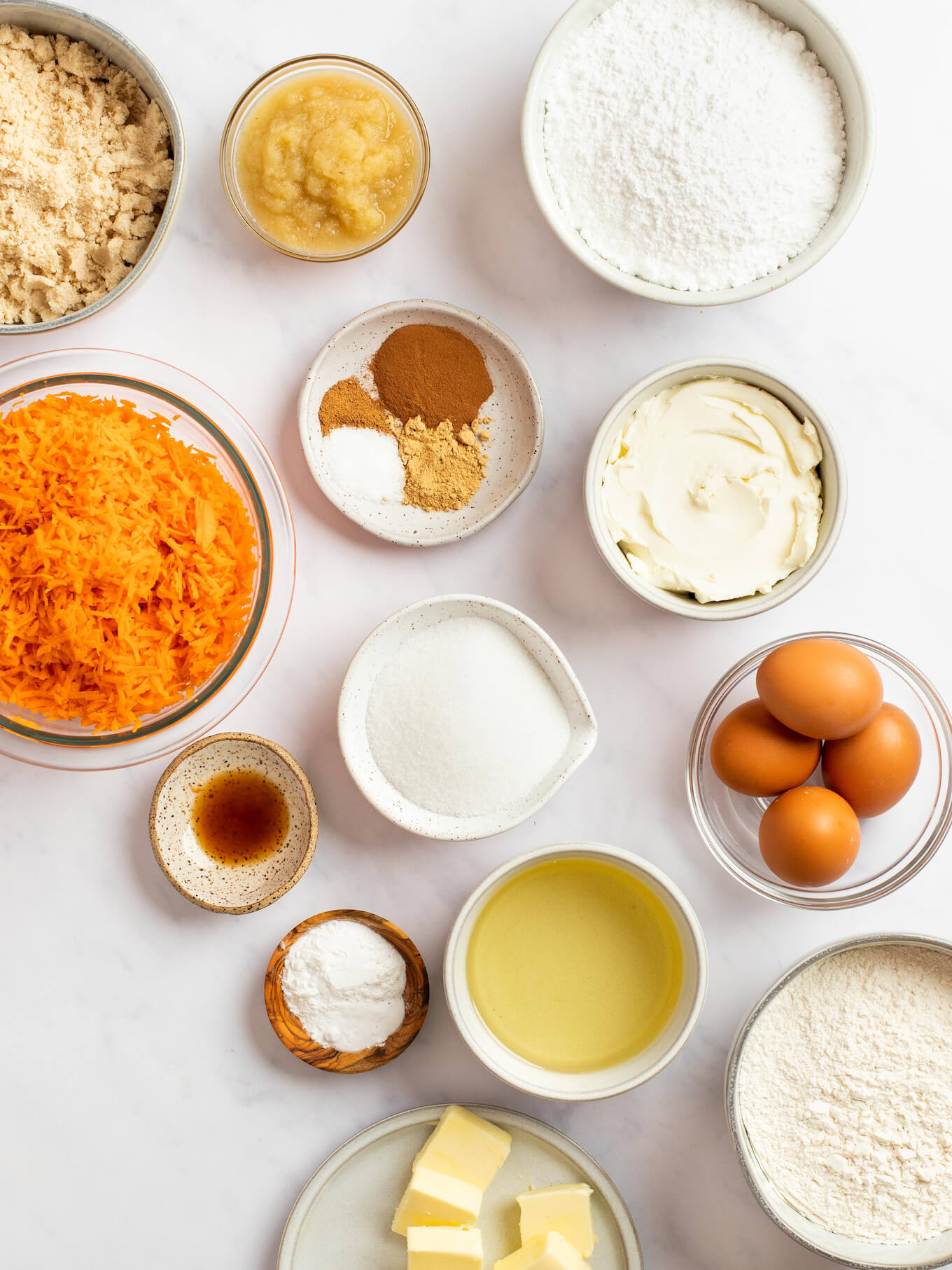 An overhead view of the ingredients for carrot cake on top of a marble surface.