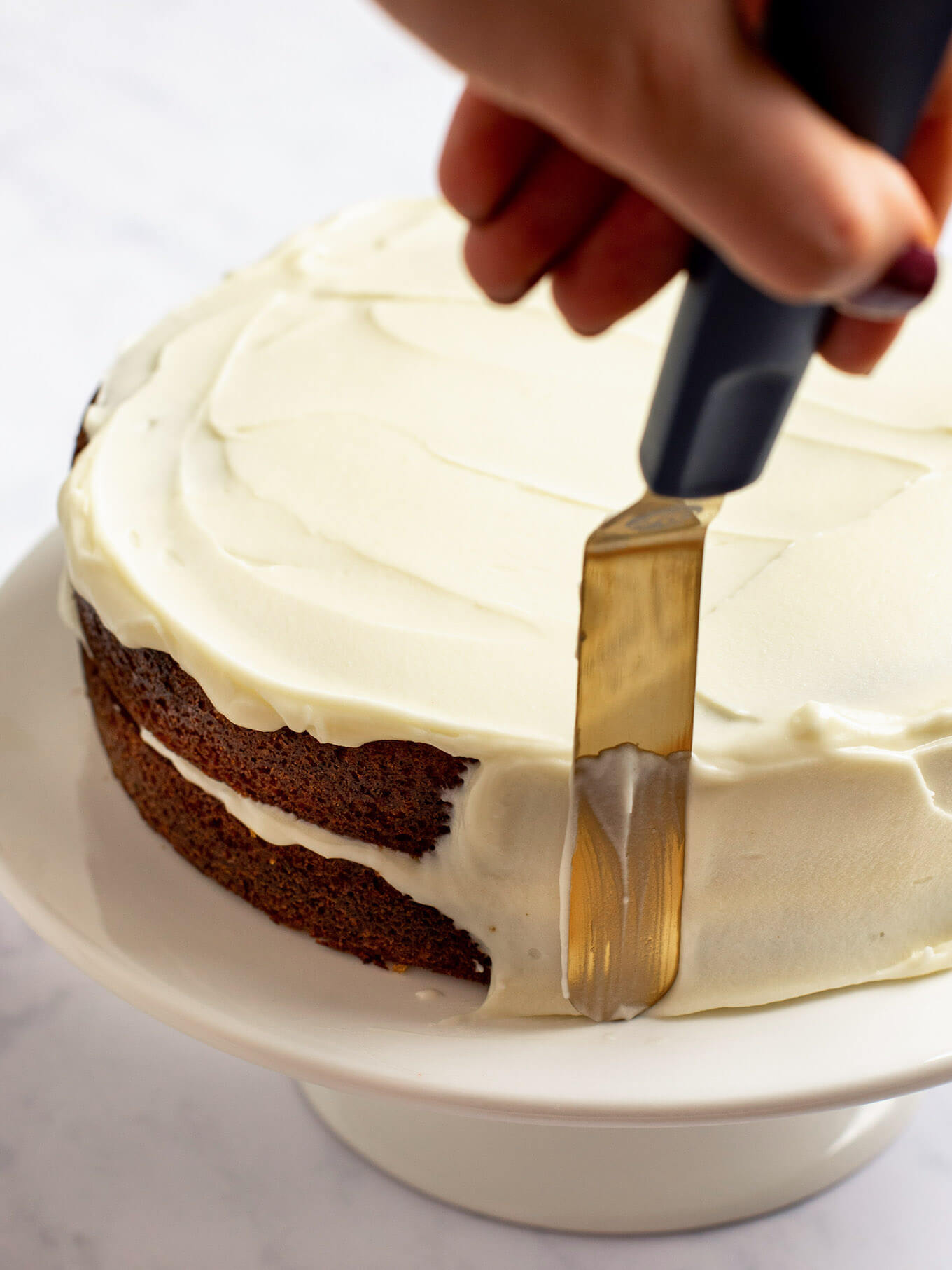 A carrot cake being frosted on the top and sides with cream cheese frosting.