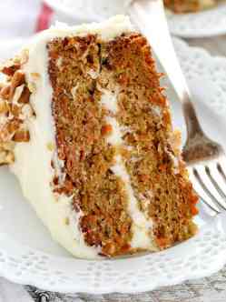 A slice of carrot cake on a decorative white plate. A fork rests on the side of the plate.