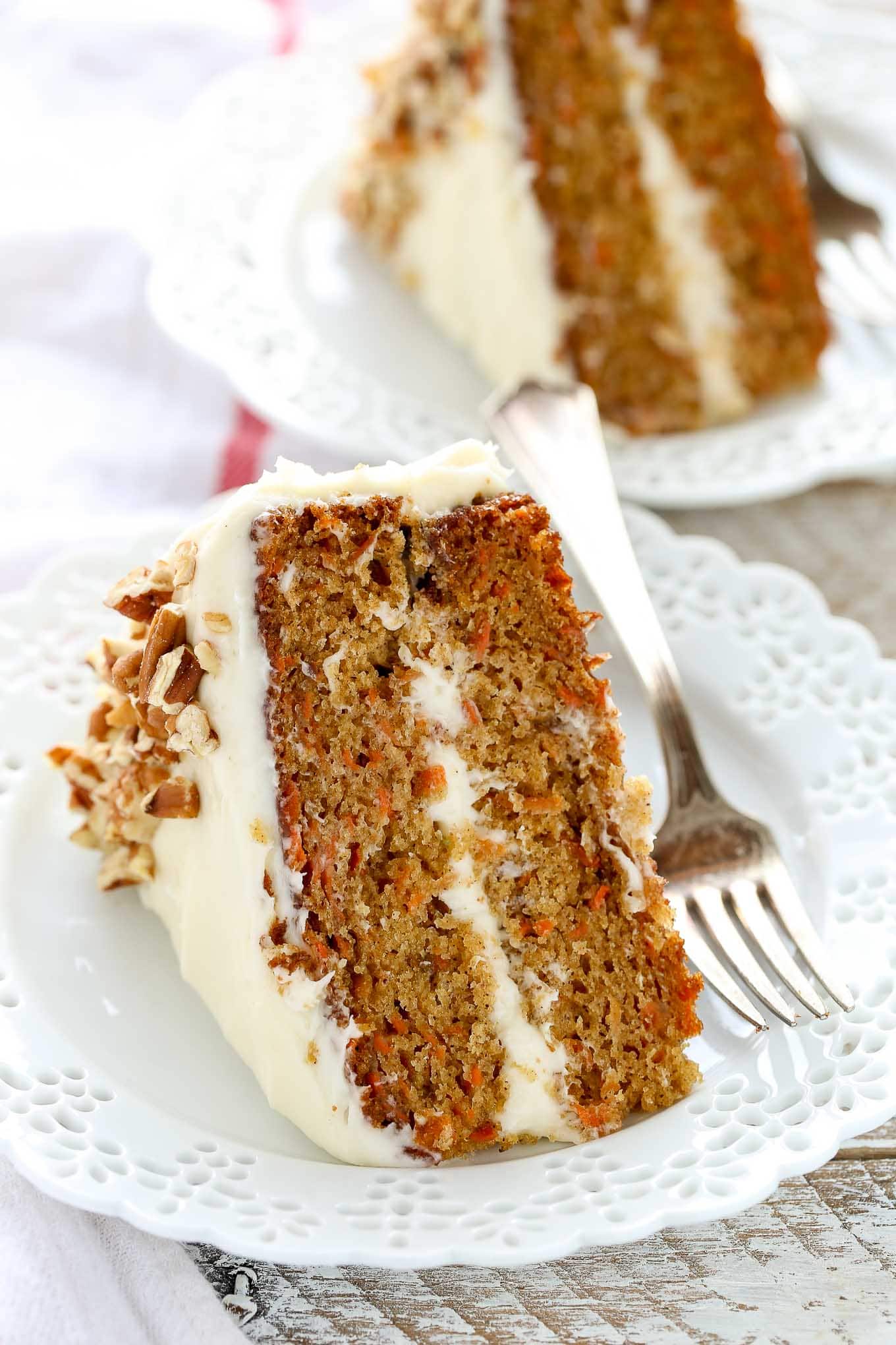 Two slices of carrot cake on separate decorative white plates. A fork rests on the side of each plate.