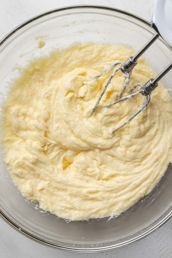 An overhead view of a butter-egg mixture in a glass mixing bowl.