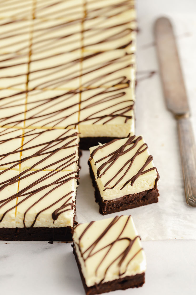 A sheet of parchment paper with cheesecake brownies cut into individual servings and two pulled out to show the layer details.