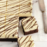 Sliced cheesecake brownies drizzled with melted chocolate on a piece of parchment paper.