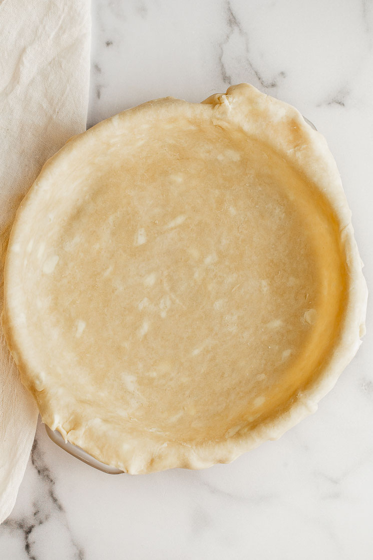 A homemade pie crust in a pie plate resting on a marble surface.