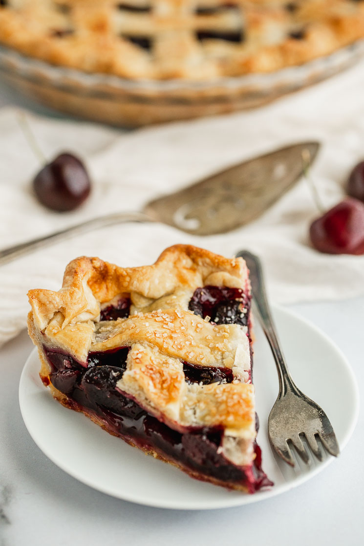 A slice of cherry pie on a white plate with an antique silver fork. 