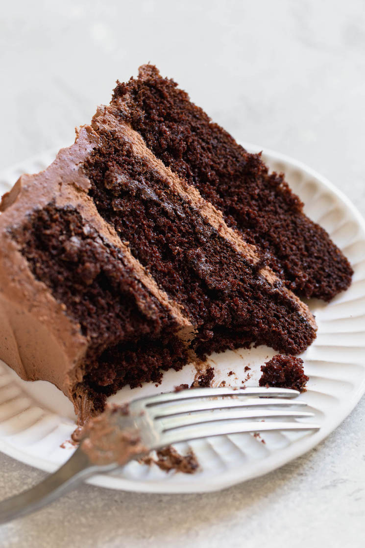 A single piece of layered chocolate cake on a plate with a bite taken out of it.