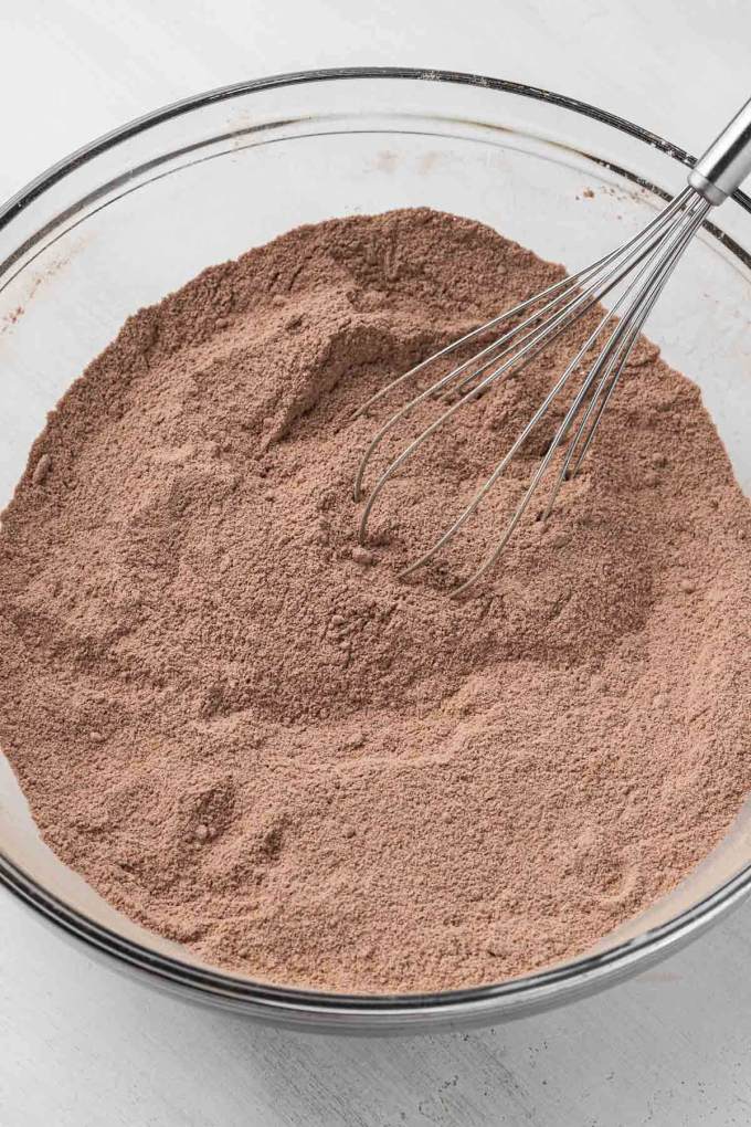 Overhead view of the dry ingredients for a chocolate cake in a glass mixing bowl with a whisk.