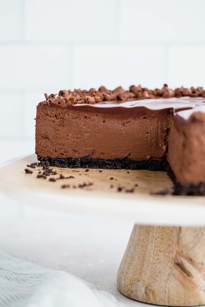 A side view of a chocolate cheesecake that's been sliced on a marble top cake stand. 