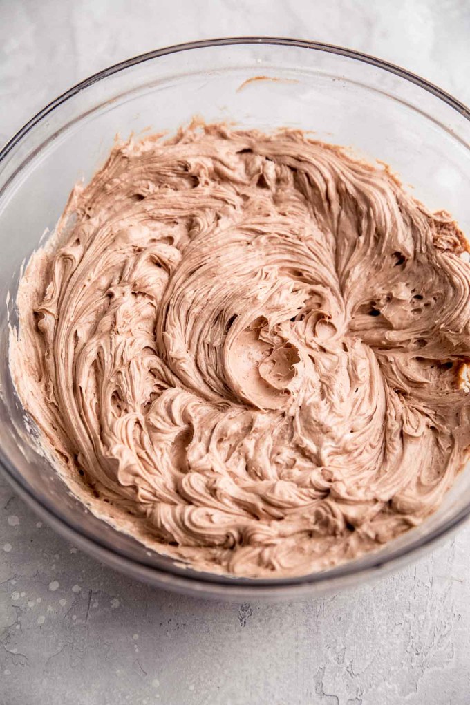 An overhead view of a chocolate cheesecake filling in a glass mixing bowl.