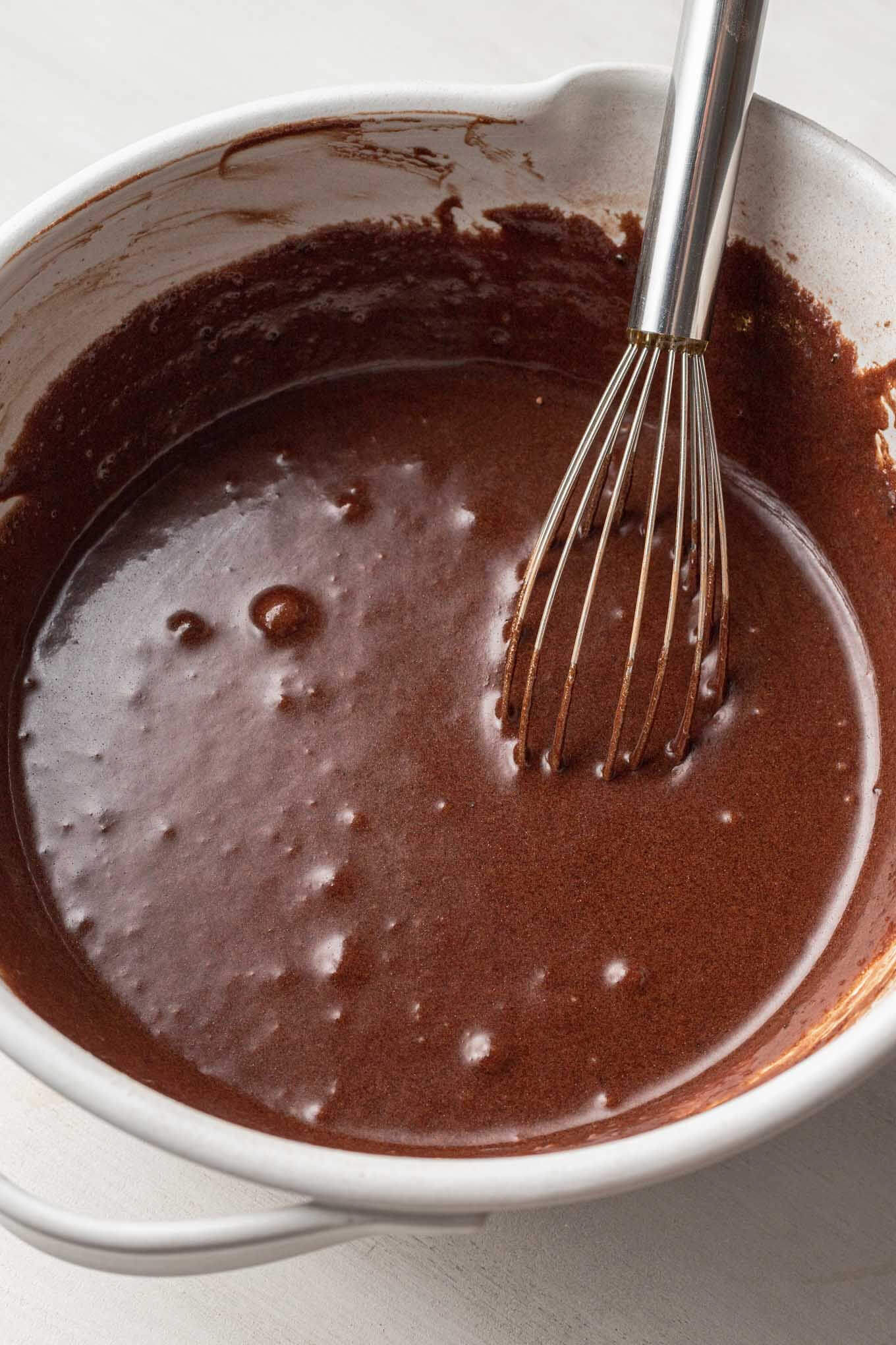 A chocolate batter in a white mixing bowl, with a whisk.