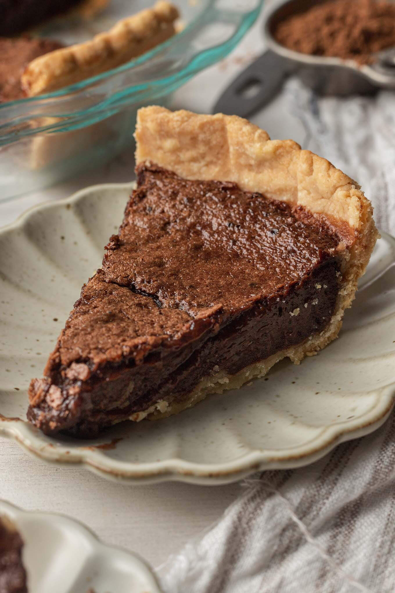 A slice of homemade chocolate chess pie on a scalloped cream plate. 