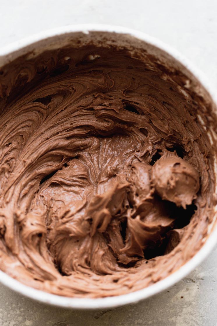 A white mixing bowl filled with chocolate buttercream frosting.