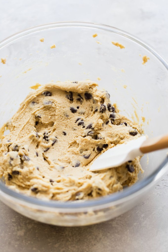 A glass mixing bowl holding finished chocolate chip cookie cake batter ready to be put in the baking pan.