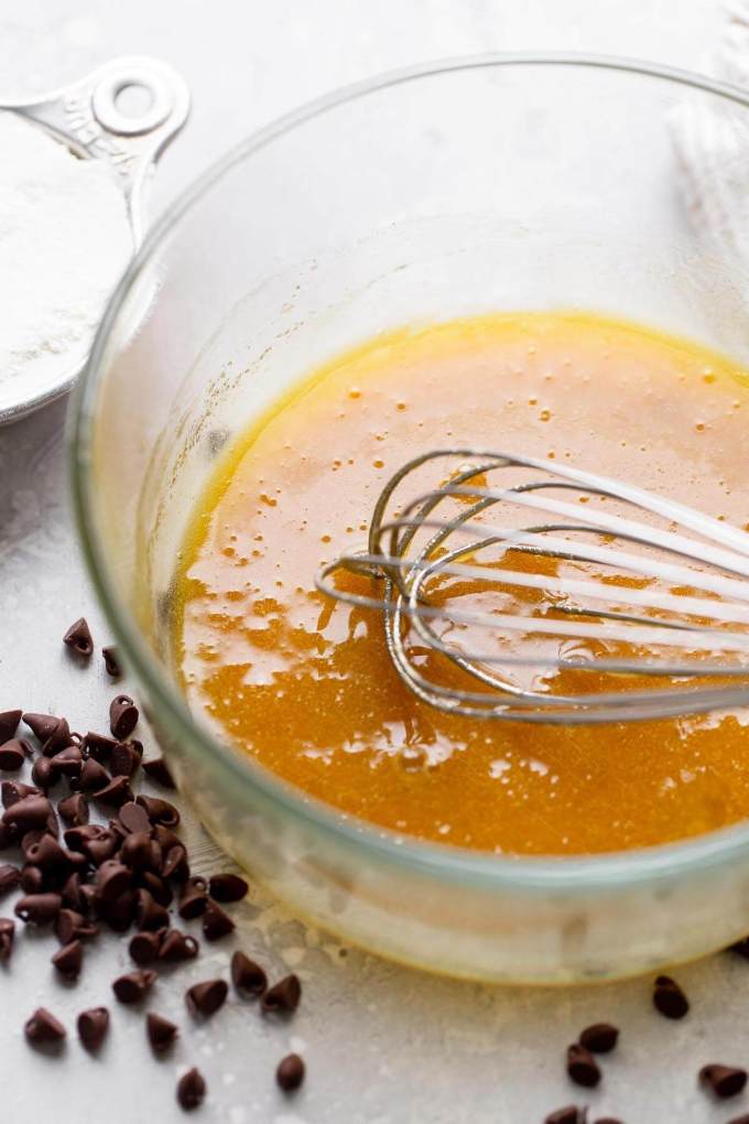 A mixture of sugar and melted butter in a glass mixing bowl, with a whisk.