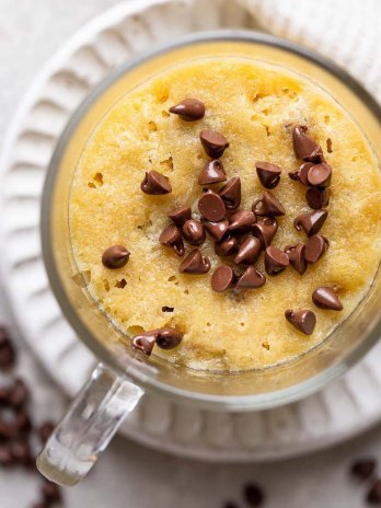 An overhead view of a chocolate chip cookie in a mug. The top of the cookie is sprinkled with mini chocolate chips.