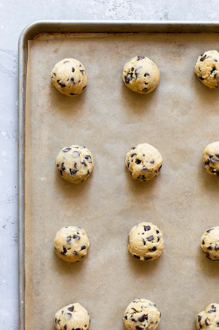 A baking sheet lined with brown parchment paper holding balls of cookie dough arranged in lines.