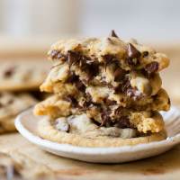 A stack of chocolate chip cookies on a white clay plate with more cookies in the background.