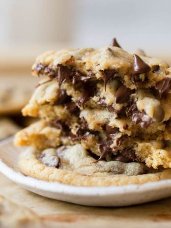 A stack of chocolate chip cookies on a white clay plate with more cookies in the background.