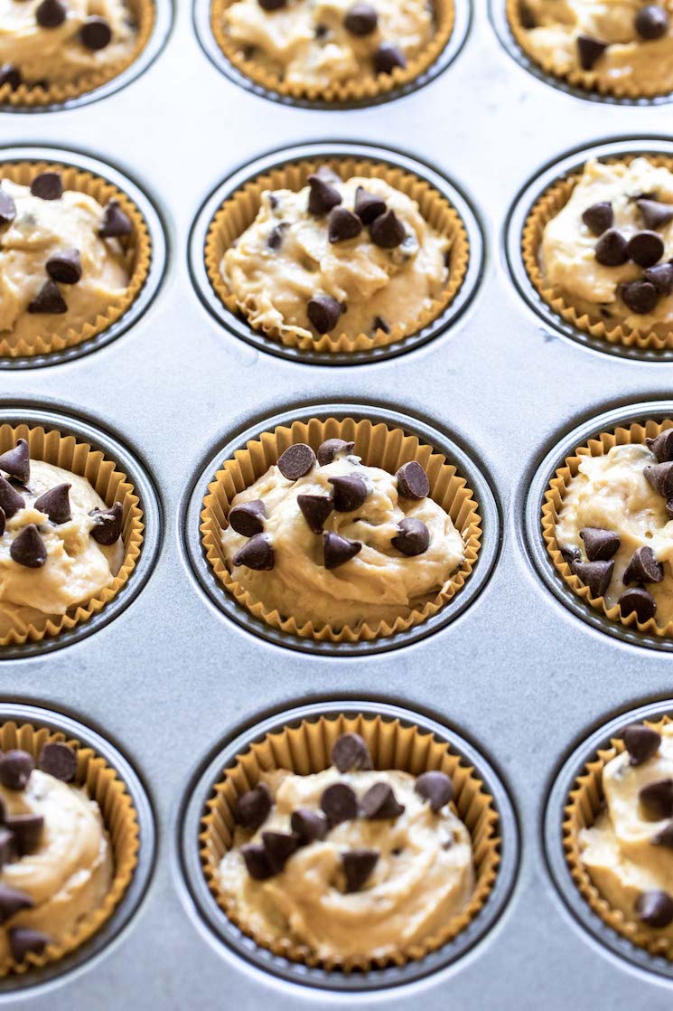 A muffin pan holding muffin liners filled with batter and topped with extra chocolate chips.