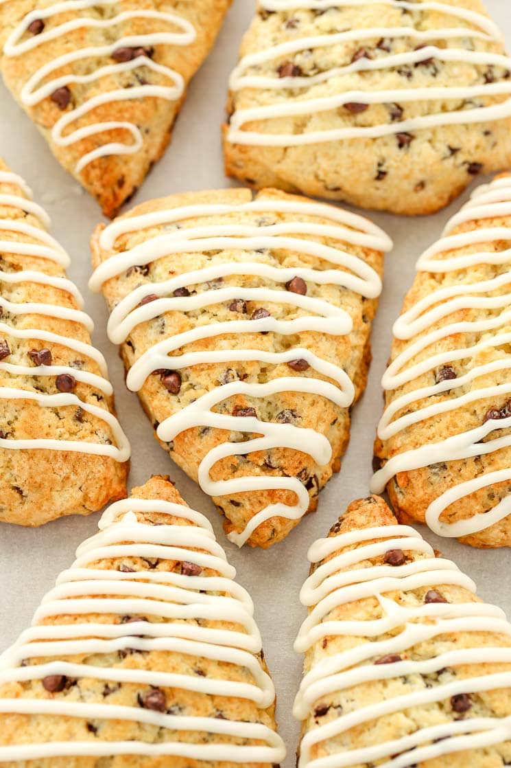 Glazed chocolate chip scones sitting on top of a piece of parchment paper.