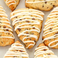 Several iced chocolate chip scones sitting on top of a piece of parchment paper.