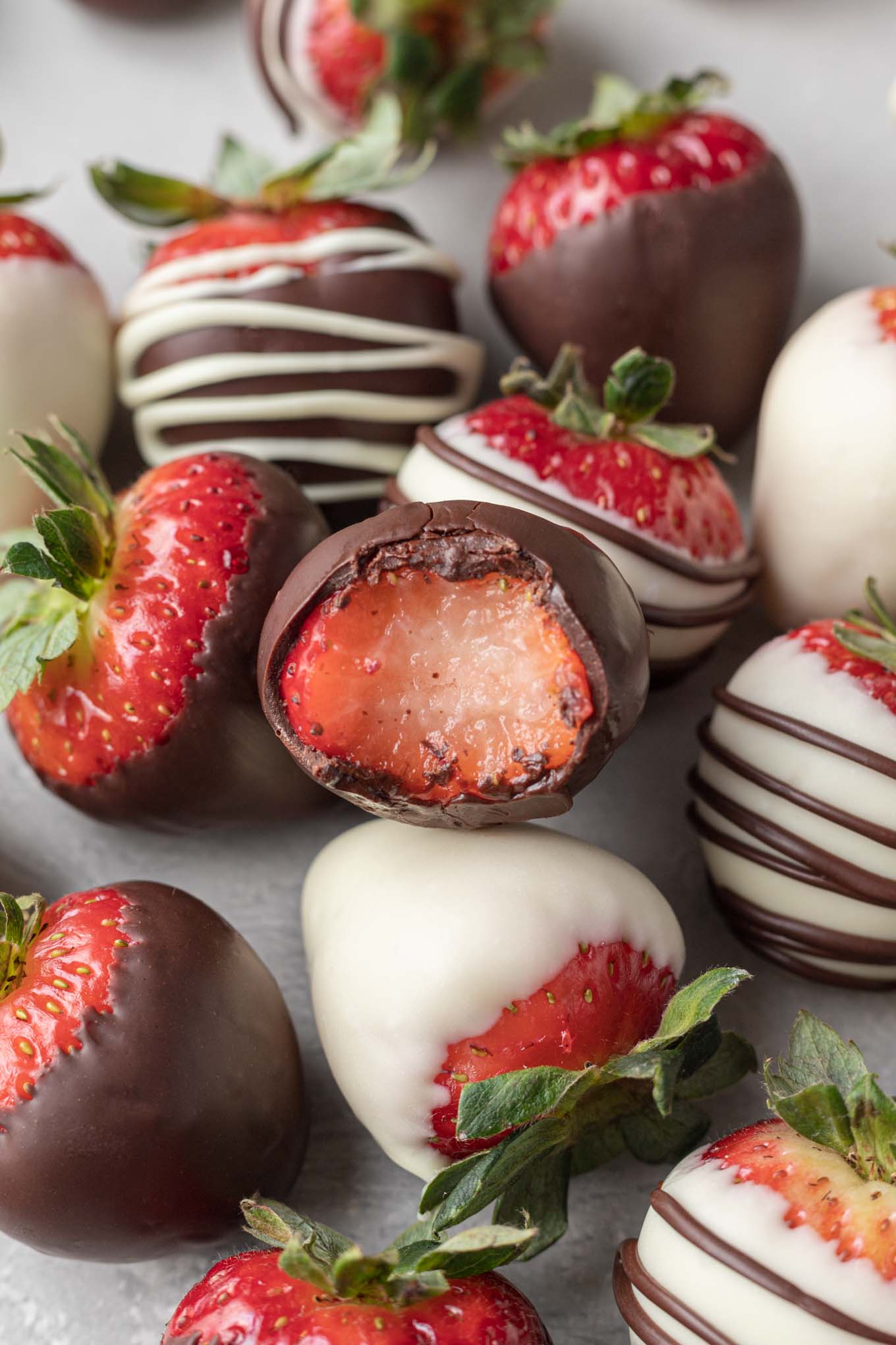 Several chocolate covered strawberries on a piece of parchment paper. One strawberry has a bite taken out of it.