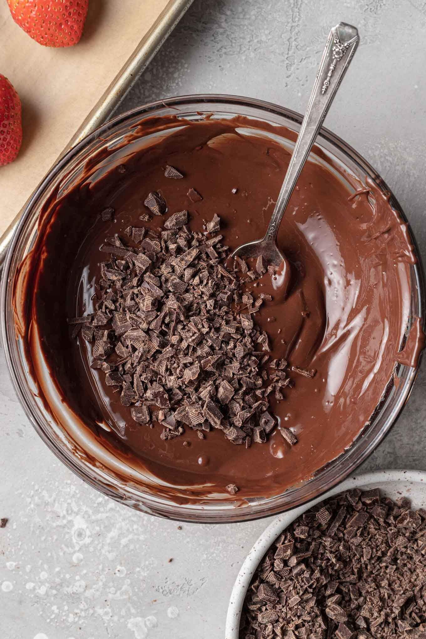 A glass mixing bowl with melted chocolate and chopped chocolate pieces.