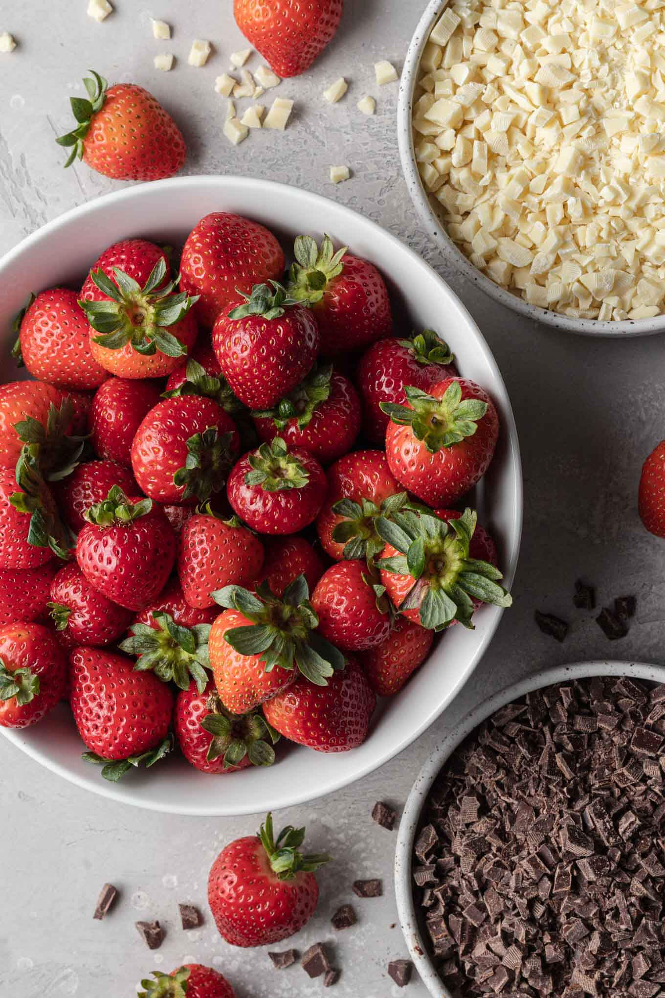 An overhead view of fresh strawberries, white and dark chocolate in separate bowls. 