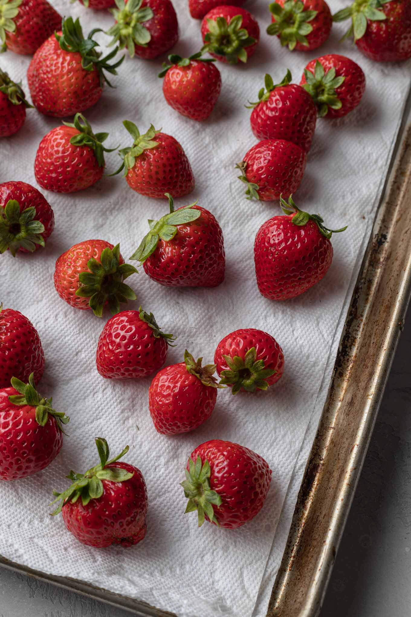 Fresh strawberries washed and left to dry on a paper towel-lined baking tray. 