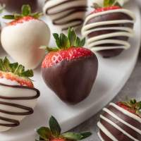 Several chocolate covered strawberries on a round piece of marble.
