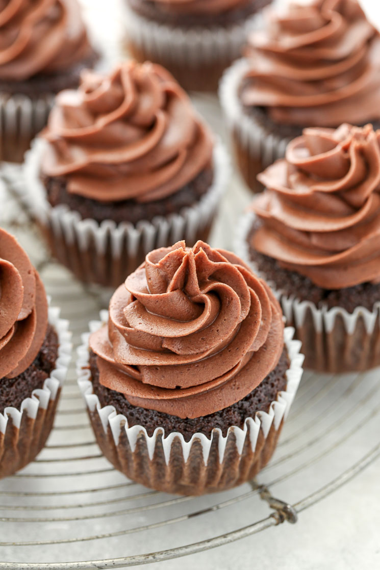 A group of chocolate cupcakes topped with chocolate cream cheese frosting sitting on top of an antique round cooling rack. 