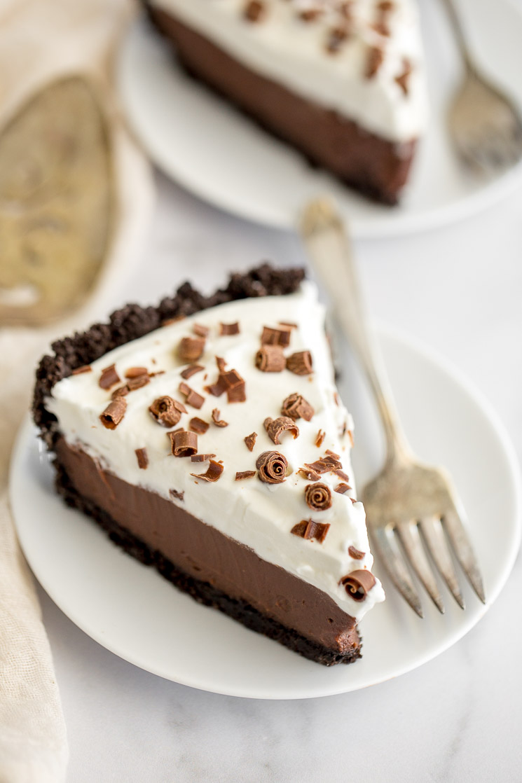 A slice of chocolate cream pie on a plate with another slice in the background.