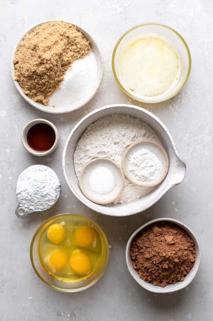 The ingredients needed to make cookies in bowls on top of a rustic gray surface.