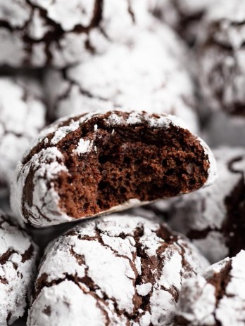 A batch of chocolate crinkle cookies with one cookie having a bite taken out of it.