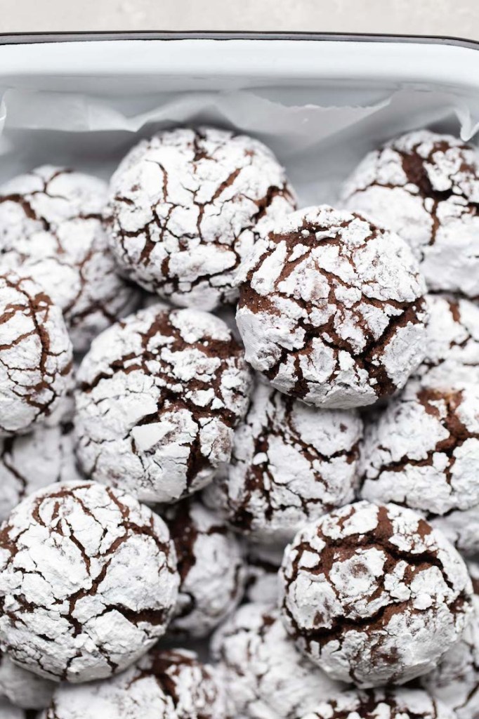 Several chocolate crinkle cookies piled on top of each other in a white dish.