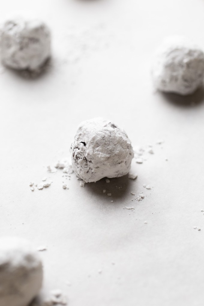 A baking sheet lined with parchment paper holding several balls of cookie dough that have been rolled in powdered sugar.