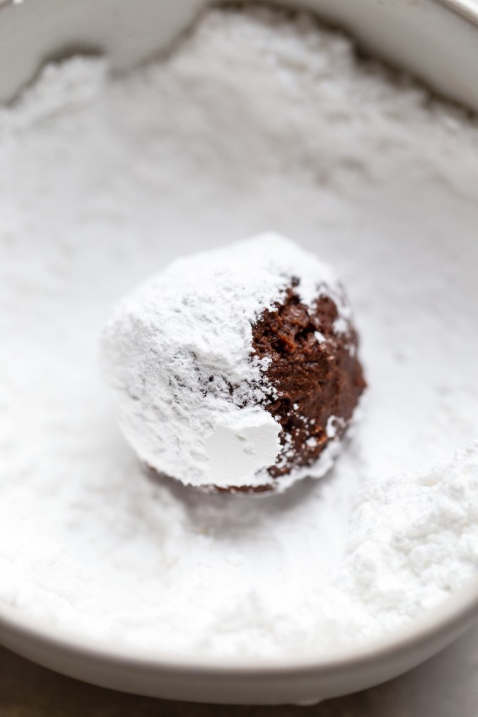 A single ball of cookie dough being rolled in powdered sugar.