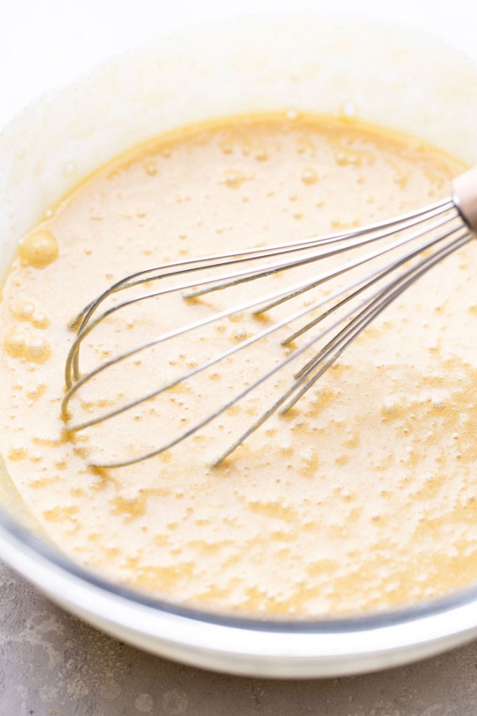 A glass mixing bowl filled with the wet ingredients being whisked together.