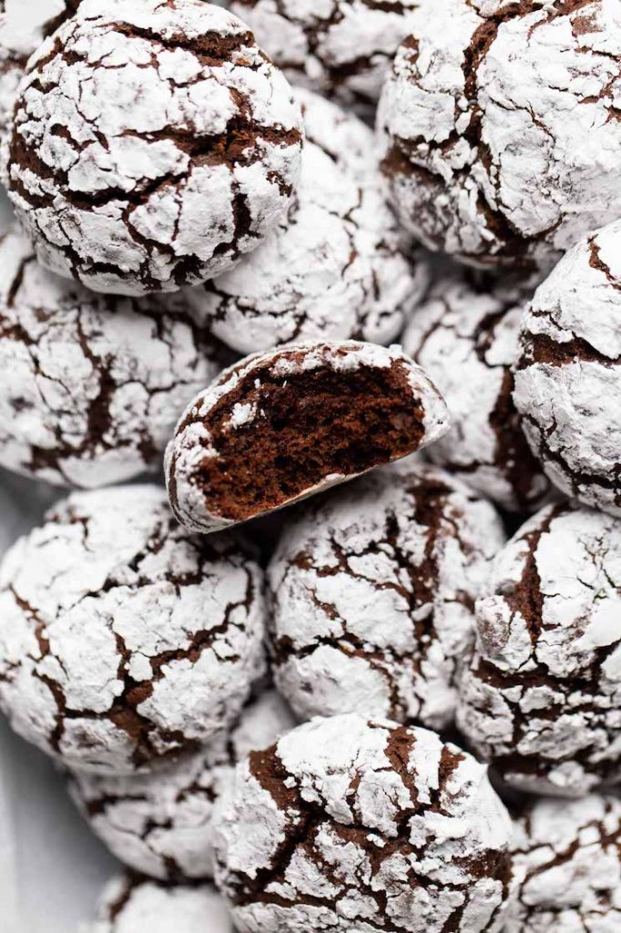 A batch of chocolate crinkle cookies piled on top of each other with a bite taken out of the top one.