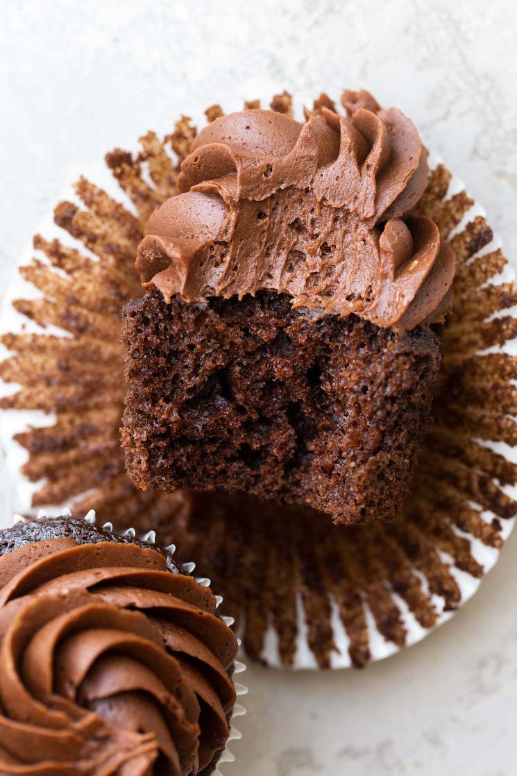 A chocolate cupcake on its side with a bite taken out to show the cake and frosting texture.