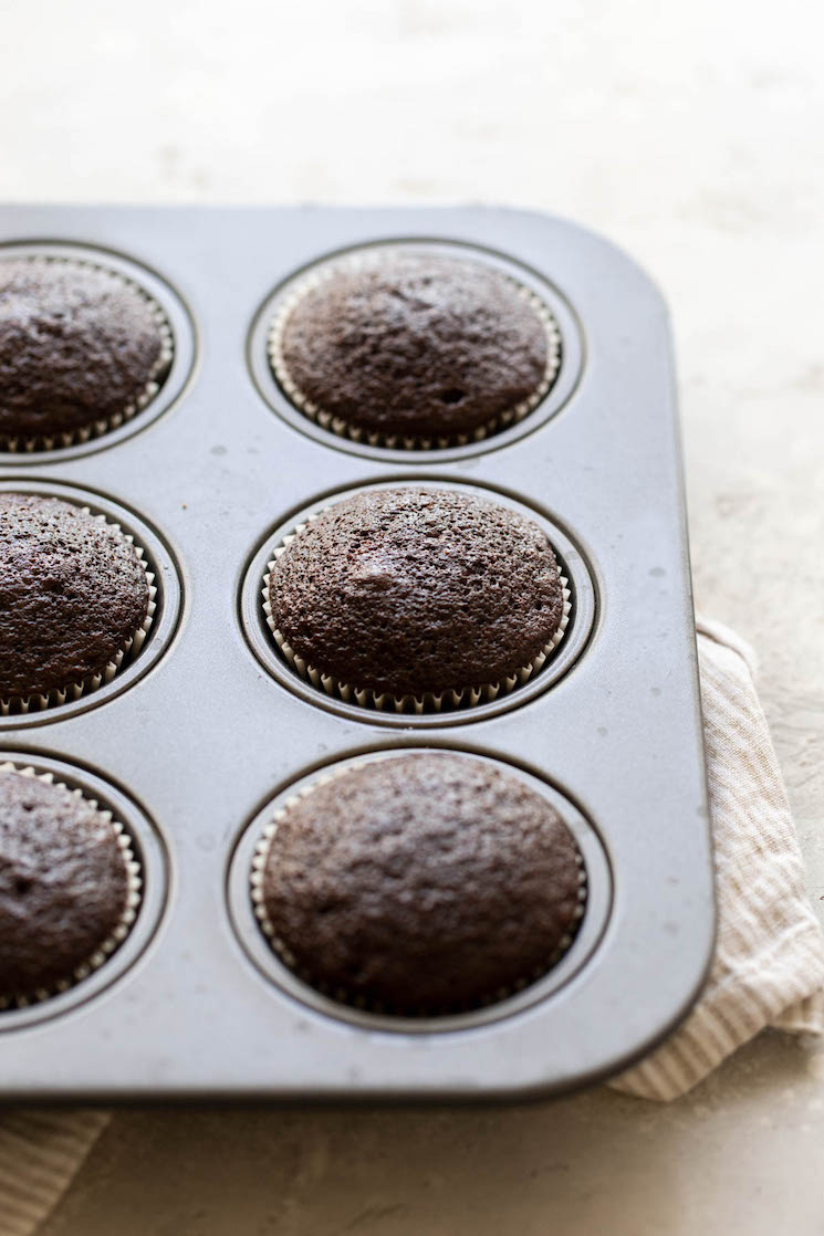 A muffin pan holding baked cupcakes on a rustic surface.