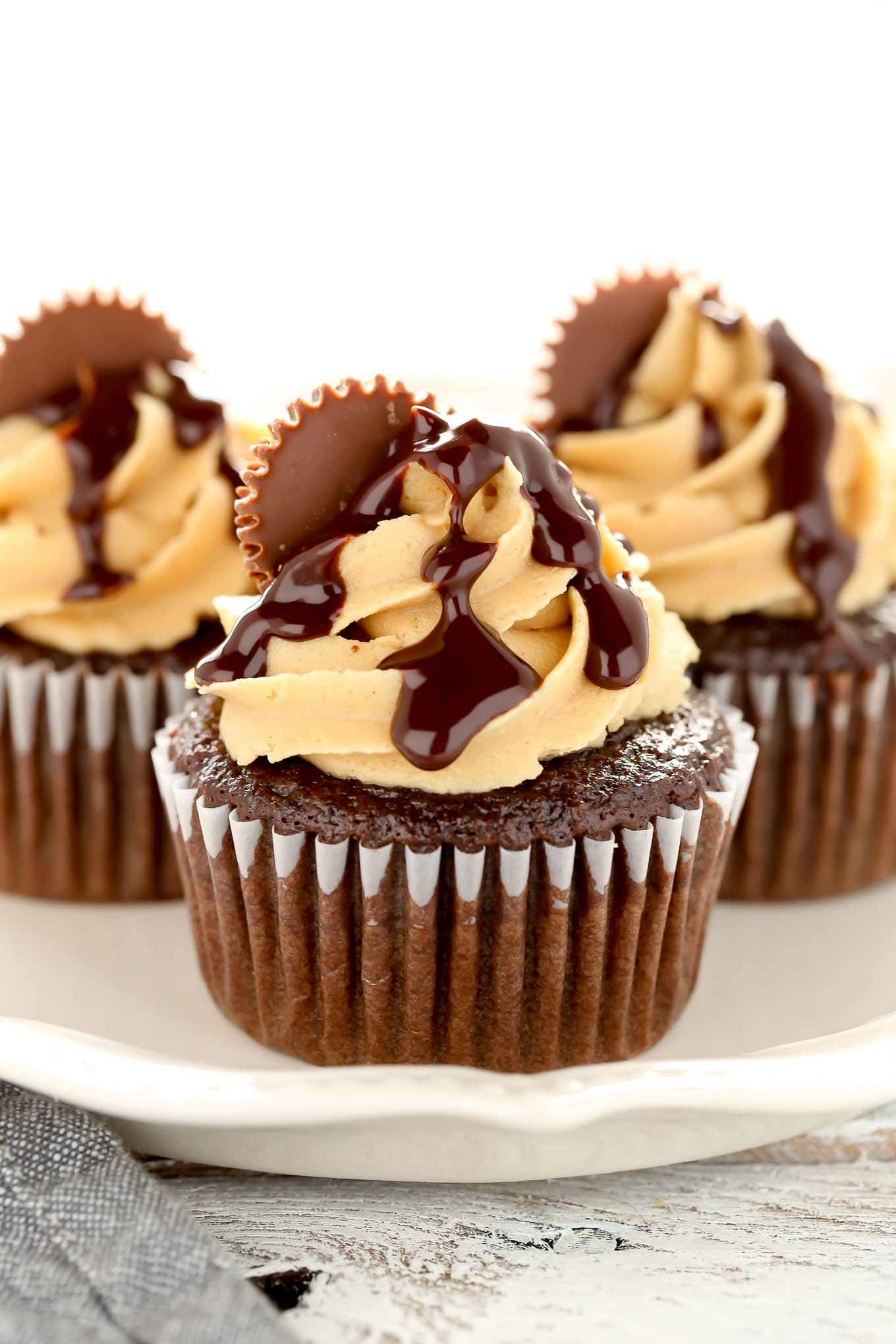 Close up of three chocolate peanut butter cupcakes on a white plate. 