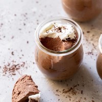 A glass jar filled with chocolate mousse topped with whipped cream and chocolate shaving with a spoonful taken out to show texture.