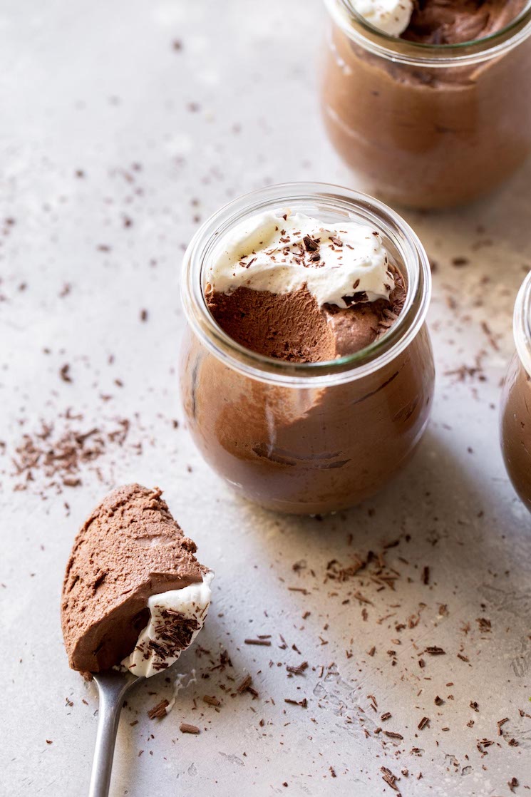 Three small jars filled with chocolate mousse topped with whipped cream and chocolate shavings.