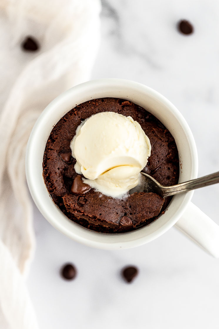 A chocolate mug cake topped with a scoop of ice cream and a bite taken out of it.